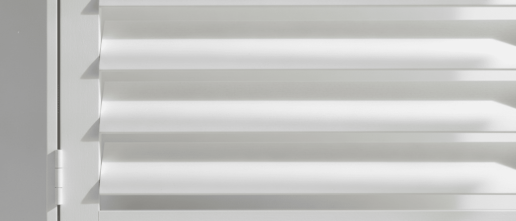 Close-up of white faux wood shutter louvres and frame, smooth painted timber-look finish, angled blades filtering